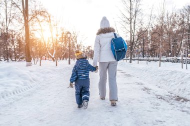Bir anne kadın çocuk evlat 2-3 yıl için el ile şehir yol boyunca kışın Anaokulundan dönen tutar. Arka, karlı yoldan görüntüleyin. Bakım desteği, ebeveyn çocuk bakımı doğru kavramı ebeveynlik.