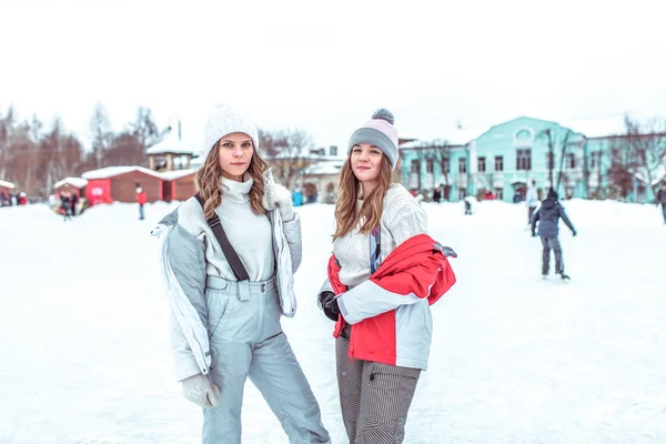 Dua siswa perempuan berpose dan tersenyum, arena seluncur es di musim dingin di taman kota. Womans beristirahat olahraga dan gaya hidup aktif. Dalam pakaian hangat musim dingin sehari-hari. Konsep liburan akhir pekan di resor musim dingin . — Stok Foto