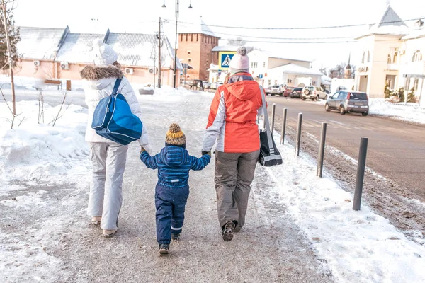 Мать-женщина с подругой родители держат мальчика сына в течение 2-3 лет вручную, зимой вдоль городской дороги. Вид сзади. Концепция по уходу за ребенком. Улица в снегу возле припаркованных автомобилей . — стоковое фото