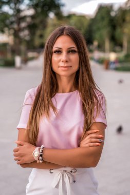 Güzel kız yaz Park. Uzun saçlı, kendinden emin ve mutlu bir görünüm. Rahat kıyafet, pembe tişört, beyaz etek.