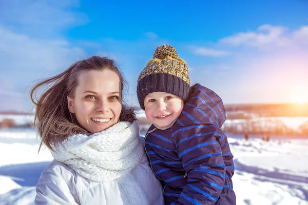 Мама с сыном на руках зимой в городе. Уход и поддержка маленького ребенка на открытом воздухе. Счастливые улыбающиеся люди отдыхают зимой в городе. Эмоции наслаждения свежим воздухом . — стоковое фото