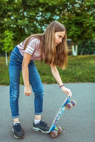 Pige teenager 9-11 år gammel, ridning et skateboard. Om sommeren i byen i afslappede jeans og sneakers. Gå i sommerparken, efter skole lektioner, hvile i byen . - Stock-foto