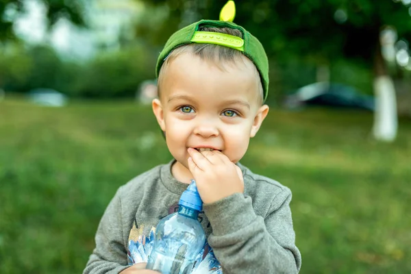 Menino de 1-5 anos, retrato de close-up, feliz rindo em suas mãos segurando uma garrafa de água. No verão na cidade ao ar livre. Um olhar sincero com olhos . — Fotografia de Stock