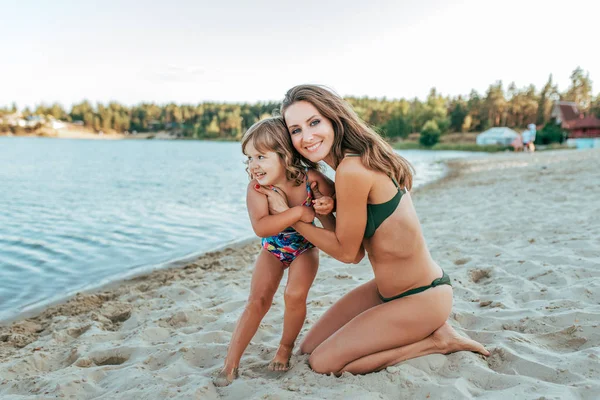 Malá holčička 2-5 let, hraje s mladou matkou na pláži v létě, venkovní resort u jezera. Happy odpočinku o víkendu. Světlé plavky na dítě. Rodiče milují, rodina a rodičovství. — Stock fotografie