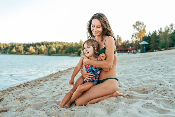 Mladá maminka si hraje s její dcera dívka 2-5 let, na pláži v létě venkovní resort u jezera. Happy odpočinku o víkendu. Světlé plavky na dítě. Rodiče milují, rodina a rodičovství. — Stock fotografie