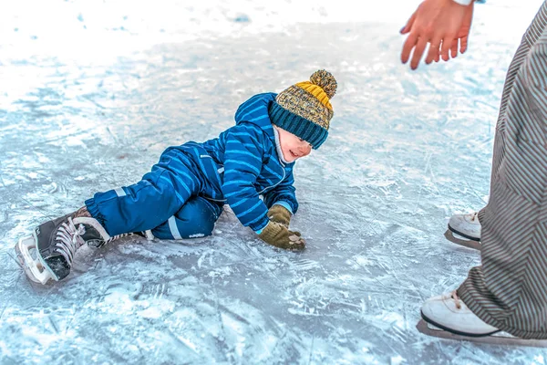 Ein kleiner Junge im Alter von 2-5 Jahren ist im Winter beim Schlittschuhlaufen auf das Eis gefallen. Mutter zieht ihren Sohn groß. glückliches Lächeln. Skaten lernen unterstützt den ersten Sturz. — Stockfoto