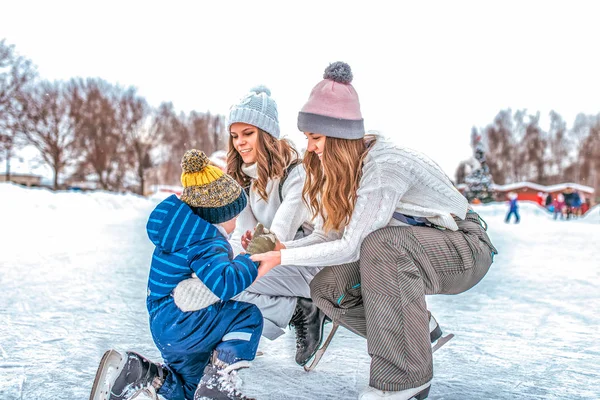 Молодая мать с подругой воспитывает маленького мальчика 4-5 лет. Коньки зимой в парке. Счастливая улыбка, катание на льду, природа молодой семьи, забота и поддержка . — стоковое фото