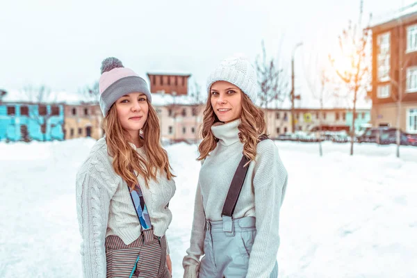 Zwei Freundinnen Studentinnen, im Winter in der Stadt, eine öffentliche Eisbahn. in lässiger Kleidung und warmen Hüten. glücklich lächelnd im Winter in der Natur entspannen. — Stockfoto