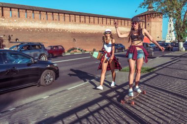 İki kız arkadaş kız, eğleniyor, longboard patenler City yaz aylarında yolda binmek. Metin için özgür yer. Oynamak ve eğlenmek temiz havada gülüyor. Yol araçları ile arka plan üzerinde.