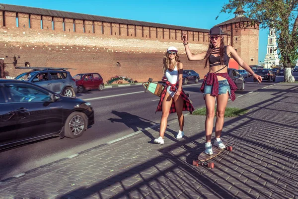 Zwei Freundinnen, die Spaß haben, fahren im Sommer in der Stadt Longboard-Skates auf der Straße. Freiraum für Text. Lachen beim Spielen und Spaß an der frischen Luft. im Hintergrund der Straße mit Autos. — Stockfoto