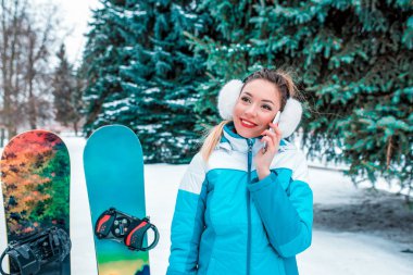 Güzel kız telefonda, kış parkta ağaçların ve snowboard arka plan üzerinde gülümseyen mutlu. Internet, mobil online başvuru üzerine söz. Metin için boş alan.