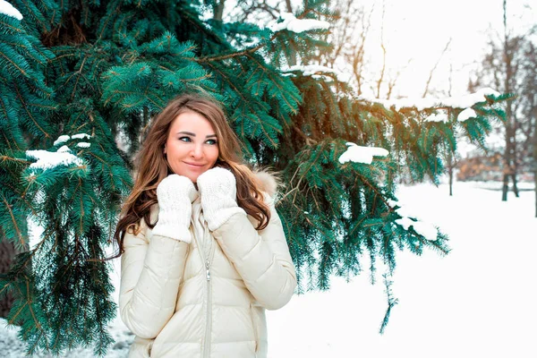 Beautiful girl in winter forest with long hair in her hands holds scarf closes her throat from cold wind outside, happy smiling dreams and dreams, against background of snow-covered Christmas trees. — Stock Photo, Image