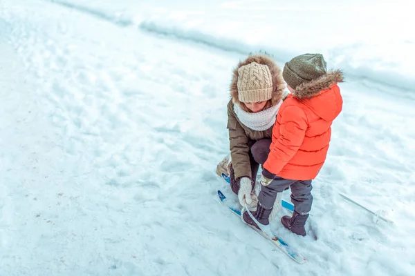 Seorang ibu muda meluruskan keterikatan bermain ski dengan anaknya selama 3-5 tahun, di musim dingin di kota terhadap latar belakang salju dan salju melayang. Ruang kosong untuk teks. Langkah pertama untuk anak ski . — Stok Foto