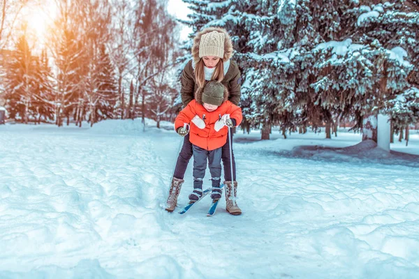 Ibu mengajari anak laki-laki berusia 3-5 tahun untuk bersepeda saat bermain ski. Di musim dingin di taman kota. Langkah pertama dari anak, olahraga, dukungan orang tua dan dukungan bagi anak . — Stok Foto