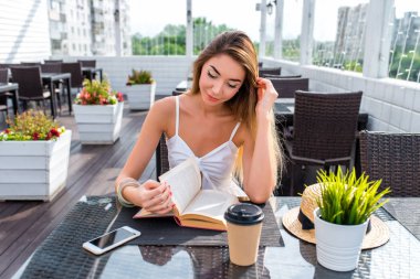 Güzel kız yazlık kafeterya, beyaz elbise tablo Restoran, kitap okuma oturma. Mutlu gülümseyen istirahat iş öğle veya akşam yemeği. Roman, dedektif hikayesi, mezuniyet öğrenme düşünceleri hayal duygu.