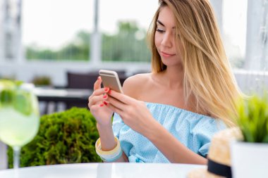 Genç ve güzel kız elbise, yakın çekim uzun saçlı mavi. Hareket eden telefon, online internet uygulaması, sosyal ağ. Okur ve telefon görünüyor. İş kadın kavramı bir yaz kafe, Restoran.