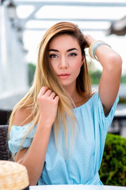 Mavi elbiseli güzel ve genç bir kadın. Bir restoran masada bir kafede yaz aylarında. Saç, hassasiyet zevk ve geri kalan duygular işten sonra düzeltir. Yakın çekim uzun saç ve rahat makyaj.