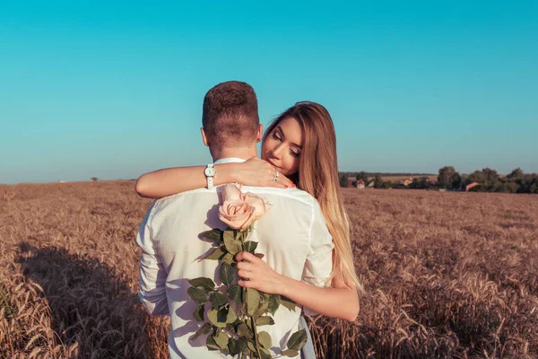 Het meisje in een jurk, hugs man man, met een boeket van roze bloemen. Het concept van de gift, de unexpectedness van liefde en vreugde. Emoties van geluk glimlach en plezier. — Stockfoto