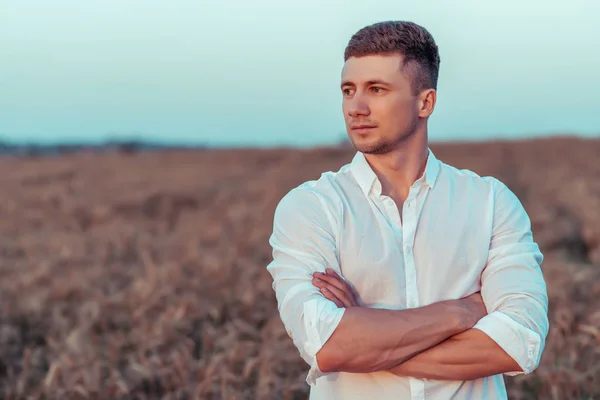 A young man in a white shirt, in the summer on wheat field, looks into the distance. Free space for text, open copy space. Emotions of self-confidence, rigor and courage.