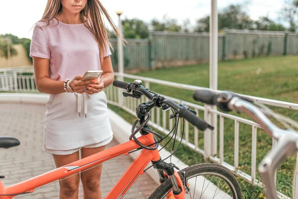 Chica sostiene la mano del teléfono móvil, fotografías bicicleta de estacionamiento. En verano aplicación de la ciudad en línea, Internet post en las redes sociales. Concepto de pérdida de bicicleta, encontrar ruta en el mapa de la ciudad, un viaje turístico . —  Fotos de Stock