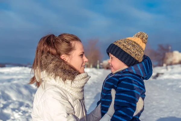 Een jonge moeder houdt de zoon van een jongen van 4-6 jaar oud, in de winter buiten op een koude dag. In de dagelijkse warme kleren en een hoed. Rust in het weekend in de natuur op een koude winterdag. — Stockfoto
