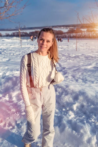 Красива дівчина в білому комбінезоні і светрі, взимку на свіжому повітрі, сніг дрейфує на фоні. У теплих рукавицях щасливий усміхнений відпочинок на природі на вихідних . — стокове фото