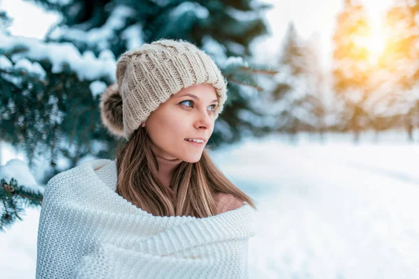 A young girl, beautiful in a white hat and rug wrapped up, warms up in the winter in the forest against the background of snow drifts and Christmas trees. Free space for text. Emotions joy smiles. — Stock Photo, Image