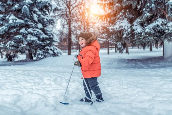 Niño de 3-5 años, en el parque en invierno pasea en esquís infantiles. Felices juegos sonrientes, primeros pasos en el deporte, espacio libre para texto. Emociones de alegría, felicidad y diversión . — Foto de Stock