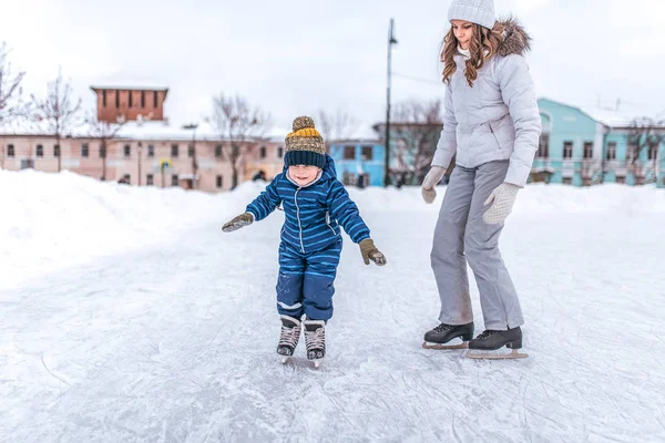 Egy fiatal anya korcsolyát parkban, télen a fiával egy fiatal gyerek 3-5 éves. Hétvége: egy nyilvános korcsolyapálya, hó és sodródik a háttérben. — Stock Fotó
