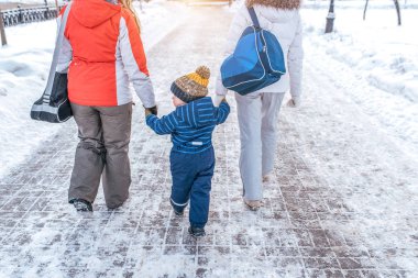 Ailem eve arkadan cevap. 3-6 yaşında küçük bir çocuk ailesi elini tutuyor. Kış aylarında kar ve snowdrifts arka plan üzerinde şehirde.