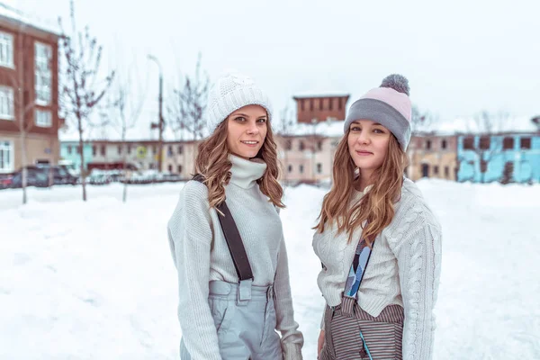 Zwei Freundinnen im Winter in der Stadt, stehen in Overalls in Pullovern und warmen Hüten auf einer städtischen Eisbahn. glücklich lächelnd, entspannend am Wochenende. — Stockfoto