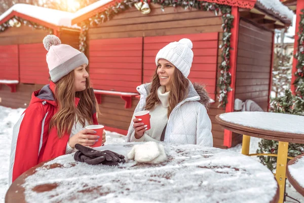 Dwie koleżanki zimy w kawiarni city na charakter na weekendy, rozmawia z filiżanki kawy i herbaty w dłoni. Szczęśliwy, odpoczynek w przyrodzie. — Zdjęcie stockowe