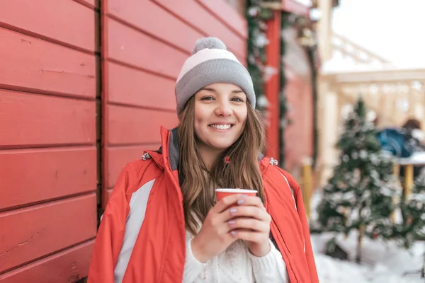 Dziewczyna z szczęśliwy uśmiechający się filiżankę kawy lub herbaty w jej ręce. Emocji, zabawy i rekreacji na świeżym powietrzu na dzień wolny w zimie w ciepłe ubrania. — Zdjęcie stockowe