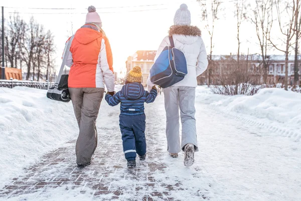 Ibu dengan anaknya, seorang anak laki-laki berusia 3-6 tahun, wanita pacar, kembali ke rumah setelah berjalan-jalan di taman di musim dingin dengan latar belakang salju dan melayang. Saling berpegangan tangan. . — Stok Foto