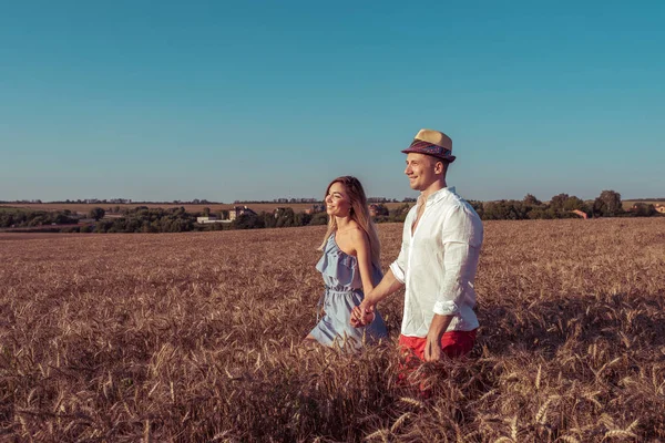 Schönes junges Paar, Mann und Frau, im Sommer auf einem Weizenfeld, sich an der Hand haltend, glücklich lächelnd. Romantische Spaziergänge auf dem Feld, Emotionen lieben Verständnis. Unterstützung glücklicher Beziehungen. — Stockfoto