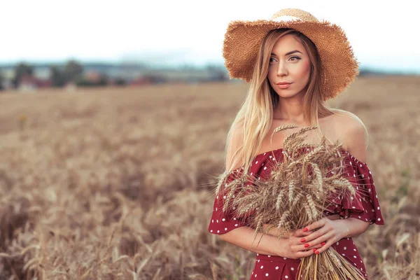 Gadis cantik gaun merah topi jerami. Di ladang gandum musim panas. Ruang kosong untuk teks. Memanen di desa, gandum ditangan. Rambut panjang kulit kecokelatan, emosi kelembutan tampilan percaya diri. Tempat untuk teks . — Stok Foto