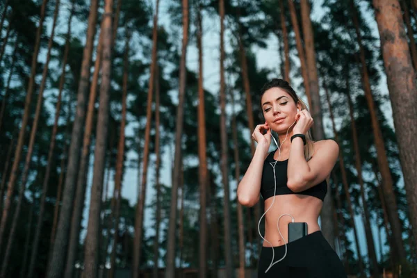 Gadis cantik atlet wanita di musim panas di hutan. Smartphone mendengarkan musik pada headphone. Ruang kosong, aplikasi internet pemain. Motivasi untuk berlari di hutan. Emosi kesenangan istirahat dan harmoni . — Stok Foto