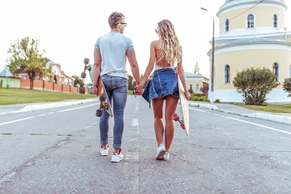 Bir genç çift kız adam yaz şehir, arka görünümünden yürüme. Kaykaylar, longboard elinde. Kavram gençler gençler, trendy ve şık rahat kıyafet içinde vardır. Hafta sonu yaşam tarzı dinlenmek.