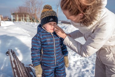 Anne sümük oğlu küçük bir çocuk siliyor. Kışın şehir bankta. Peçete, sıcak giysiler içinde. Hafta sonu tatil dinlenmek.