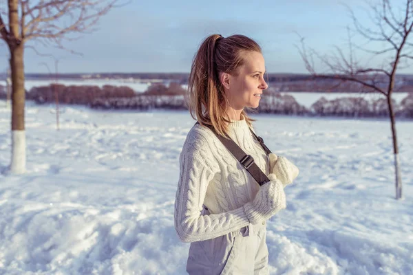 Uma jovem no inverno na cidade está contra o pano de fundo de neve e árvores. Espaço livre para texto. Em macacões brancos e luvas quentes . — Fotografia de Stock