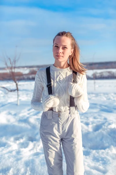 Indah musim dingin wanita dalam jumpsuit putih dan sarung tangan hangat. Berpose di kota dengan latar belakang salju dan salju melayang pada musim dingin Februari dan Januari . — Stok Foto