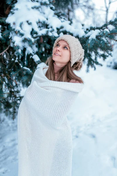 Een gelukkig meisje in de winter in het bos, in de witte trui en warme muts, kijkt naar de top. Tegen de achtergrond van sneeuw en groene bomen in de sneeuw. Camping resort in januari februari. — Stockfoto