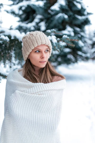 Uma mulher bonita no inverno na floresta, com uma camisola branca e chapéu quente, olha para o lado. Contra o fundo da neve e árvores verdes na neve. Menina descansando na natureza resort em janeiro fevereiro . — Fotografia de Stock