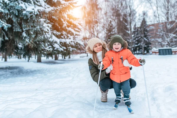 Frau Mutter hilft ihrem Kind, Junge von 3-6 Jahren, stehen Kinderski, Freude Lächeln Spaß. Erste Schritte beim Skifahren. Unterstützung, Lernen eines gesunden Lebensstils. im Winter im Stadtwald. Freiraum für Text. — Stockfoto