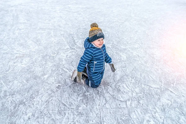 Маленький мальчик 4-6 лет, на коленях, катается на коньках, зимой в городе на катке. Счастливая улыбка, пытаясь проехать первые шаги на катке. Свободное место для текста . — стоковое фото