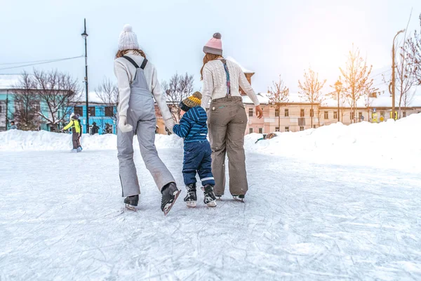 Родители маленького мальчика катаются на коньках, вид сзади, девушки подружки, учат сына 3-5 лет, катаются на коньках зимний парк. Уроки поддержки и ухода, первые шаги спорта . — стоковое фото