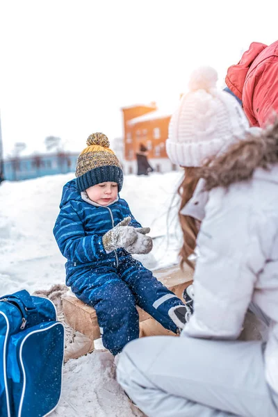 Маленький мальчик 4-6 лет, сидит на скамейке, зимой в городе на катке. Жду, когда мама наденет коньки. В холодный день по выходным в январе . — стоковое фото