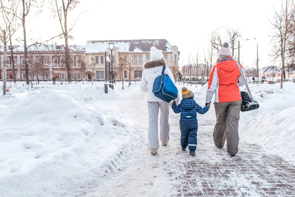 Két barátnő kis fiú 3-5 éves, téli város ellen hátteret hó és a hóban sodródik, nézze meg a hátsó, vissza haza edzés után pihenésre a park, a skate táskák szabadnap. Szabad hely a szöveg. — Stock Fotó