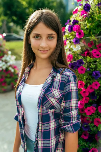 Mädchen Teenager schöne 11-14 Jahre auf dem Hintergrund eines Blumenbeetes. glückliches Lächeln. im Sommer in der Stadt nach der Schule. Ferienwochenende in der Stadt. Hemd T-Shirt. Emotionen der Freude, des Spaßes, des Lebensstils. — Stockfoto