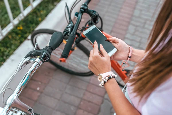 Close-up tangan gadis smartphone. Di kota musim panas latar belakang parkir untuk sepeda, gadis memilih rute dalam aplikasi, peta internet online di telepon. Rute jalur sepeda. Parkir sepeda di kota . — Stok Foto